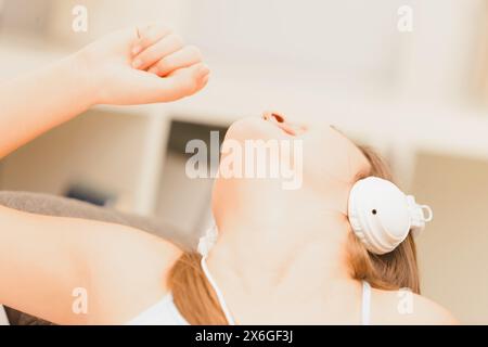 Die junge Frau singt fröhlich in ihrem Wohnzimmer, mit Kopfhörern, und spürt den Rhythmus ihrer Lieblingsmusik Stockfoto