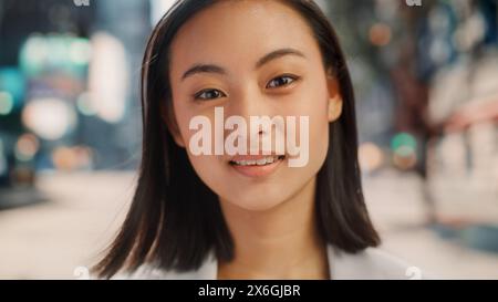 Porträt einer schönen japanischen Frau, die elegante Freizeitkleidung trägt und auf der Straße posiert. Erfolgreiche Frau in Big City, die den urbanen Lebensstil lebt. Hintergrund mit Bürogebäuden und Reklametafeln. Stockfoto