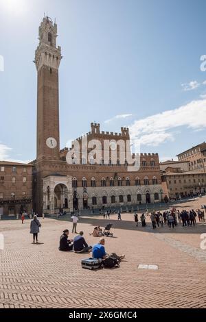 Touristen saßen an einem sonnigen Tag mit blauem Himmel auf der berühmten Piazza del Campo in der historischen mittelalterlichen Stadt Siena in der Toskana. Stockfoto