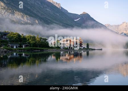 Historisches Holzgebäude im alten Stil am Rande eines Bergsees, umgeben von Nebel und Bäumen, viele Glacier Hotels, Swiftcurrent Lake, GL Stockfoto