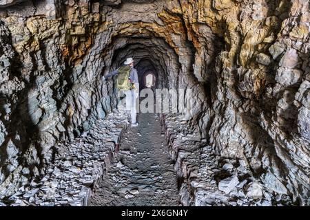 Reife Caucasian man Wanderer steht in einem Fußgängertunnel, der durch Red Argillith und Quarzitgestein gesprengt wurde, Ptarmigan Tunnel, Glacier National Park, Stockfoto