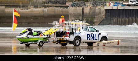 Ein Panoramabild eines RNLI Rettungsschwimmers, der auf einem Rettungswagen sitzt, der am Towan Beach in Newquay in Cornwall in Großbritannien geparkt ist. Stockfoto