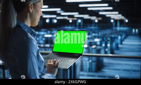 IT-Spezialist, die Chroma Key Notebook im Rechenzentrum verwendet. Big Server Farm Cloud Computing Facility mit Wartungstechniker, der mit Green Screen-Computer arbeitet. Stockfoto