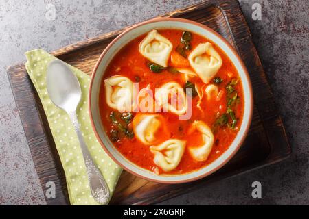 Köstliche cremige Tomaten-Tortellini-Suppe mit Spinat und Gemüse auf dem Teller auf dem Tisch. Horizontale Draufsicht von oben Stockfoto