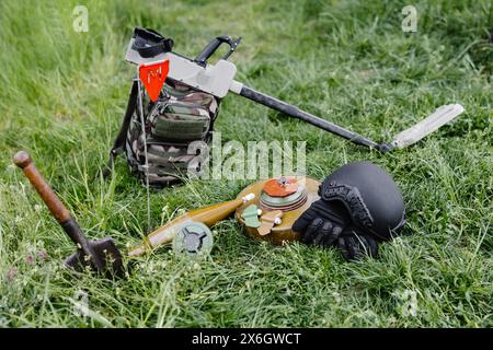 Sprengkörper und ein Metalldetektor liegen auf dem Hintergrund eines Waldmassivs. Ausrüstung für die Minenräumung des Gebiets. Stockfoto