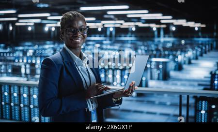 Rechenzentrum: Programmiererin mit Laptop-Computer, lächelnd und in die Kamera schaut. In Cloud Computing Server Farm System Administrator arbeitet an IT Maintenance für IaaS, saas, paas. Stockfoto