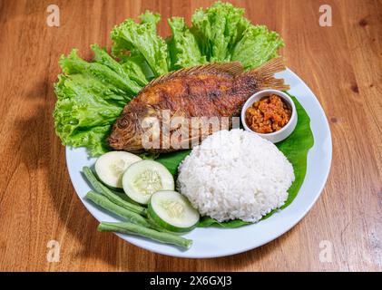 Frittierte Tilapia oder Ikan Nila Goreng serviert mit Salat, Gurke und Sambal auf Teller Stockfoto