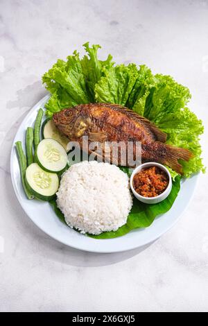 Frittierte Tilapia oder Ikan Nila Goreng serviert mit Salat, Gurke und Sambal auf Teller Stockfoto