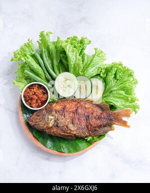 Frittierte Tilapia oder Ikan Nila Goreng serviert mit Salat, Gurke und Sambal auf Teller Stockfoto