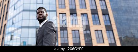 Selbstbewusster, seriöser afroamerikanischer Geschäftsmann, der vor einem modernen Bürogebäude steht Stockfoto