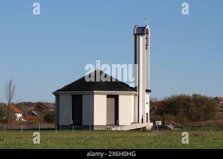 Neu gebaute moderne, weiße und graue katholische Kirche hoher Glockenturm mit eisernem Kreuz auf der Oberseite und großem klingelnden Glockenmechanismus in der Mitte Stockfoto