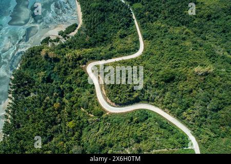 Aus der Vogelperspektive auf die gewundene Landstraße, die durch grüne Hügel führt. Sommer- und Reiseurlaubskonzept. Stockfoto