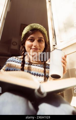 Eine trendige Frau zeigt ihre vom Hippie inspirierte Mode vor dem malerischen Blick auf den Park, mit einem Trailer im Hintergrund. Stockfoto