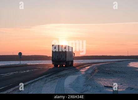 Semi-Truck fährt auf einer verschneiten Autobahn bei Sonnenuntergang im Winter Stockfoto