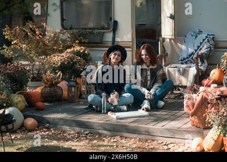 Zwei stylische Mädchen in Hippie-Kleidung posieren vor dem Hintergrund eines Trailers. Stockfoto