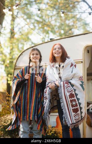 Zwei angesagte Mädchen zeigen ihre Hippie-inspirierten Outfits im Trailer-Setting. Stockfoto