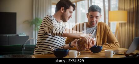 Zwei gutaussehende Freunde essen buntes Frühstückszerealien in der gemütlichen Küche im stilvollen Apartment. Junge Erwachsene Schwule Paare haben ein Gespräch beim Essen gesunde nahrhafte Nahrung am Morgen. Stockfoto