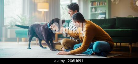 Im stilvollen Apartment zu Hause: Happy Gay Pair Play with their Dog, wunderschöne Brown Labrador Retriever. Boyfriends necken, Haustier und Kratzer Super Happy Doggy, viel Spaß in der Wohnzimmer Wohnung. Stockfoto