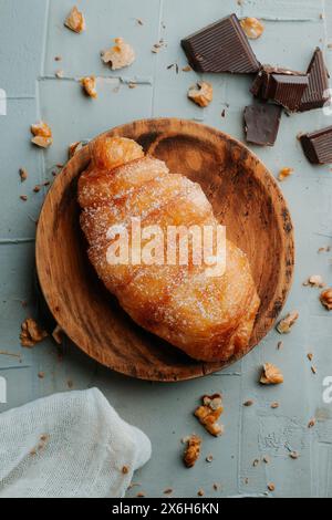 Blick aus einem hohen Winkel auf ein xuixo de Crema, ein typisches Gebäck kataloniens, spanien, gefüllt mit Pudding, auf einem Holzteller, auf einer strukturierten grauen Oberfläche Stockfoto