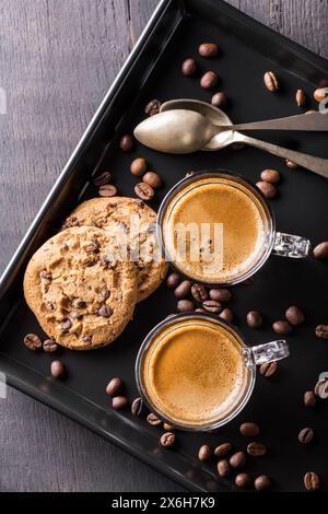 Auf dem schwarzen Tablett, im Vordergrund, zwei duftende Kaffees in Glasbechern und Schokoladenkekse Stockfoto