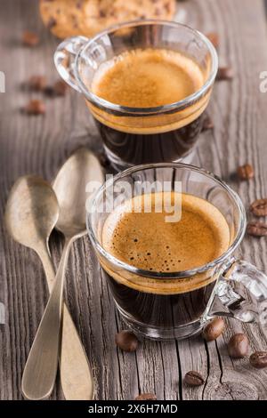 Auf dem rustikalen Holztisch, im Vordergrund zwei duftende Kaffees in Glasbechern, Stockfoto