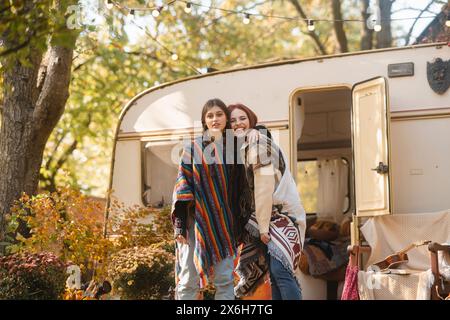 Zwei stylische Mädchen in Hippie-Kleidung posieren vor dem Hintergrund eines Trailers. Stockfoto