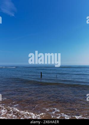 2 alte hölzerne Netzpfosten bei Ebbe am Elliot Beach in der Nähe von Arbroath mit kleinen Wellen, die über das klare Wasser Rollen Stockfoto