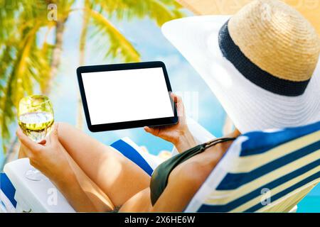 Frau, die ein digitales Tablet mit leerem Bildschirm hält, während sie sich im Resort auf einen Liegestuhl legt. modell Stockfoto