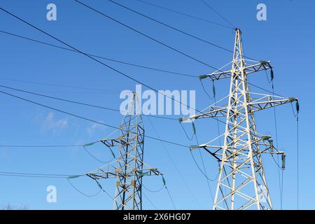 Hochspannungsmasten stehen hoch vor einem klaren blauen Himmel und tragen elektrische Kabel über die Landschaft. Stockfoto