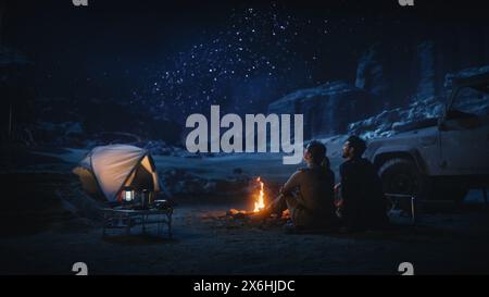 Happy Pair Zelt Camping im Canyon, am Lagerfeuer sitzen und den Nachthimmel mit der Milchstraße voller heller Sterne beobachten. Zwei verliebte Reisende auf einem romantischen Urlaub. Rückansicht Aufnahme Stockfoto