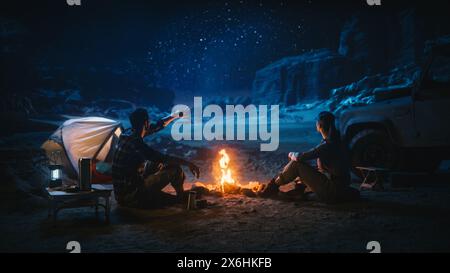 Schönes junges Paar, das am Lagerfeuer sitzt und beim Camping im Canyon den Nachthimmel beobachtet. Freundin und Freund Erzählen inspirierende Naturgeschichten über das Leben, sehen Sie sich die Milky Way Stars an Stockfoto