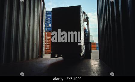 Gabelstaplerfahrer Be- oder Entladen eines Transportladungsbehälters mit einer vollen Palette mit Kartonboxen im Logistics Operations Port Terminal. Schuss aus dem Inneren des Containers, Stockfoto