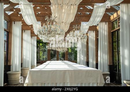 Der lange Tisch mit weißer Tischdecke steht unter dem Baldachin und luxuriösen Kronleuchtern an sonnigen Tagen Stockfoto
