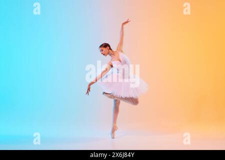 Die anmutige und kompetente junge Balletttänzerin spielt Tanzbewegungen in Aktion im Neonlicht vor blau-orangem Hintergrund. Stockfoto