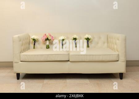 Schicke Hochzeitssträuße auf einer weißen Ledercouch - elegantes Blumendesign Stockfoto