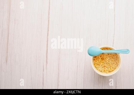 Übersicht über eine Schüssel Instant Nudelsuppe mit einem Löffel hellblau auf weißem Hintergrund. Mittagessen. Fastfood-Konzept Stockfoto