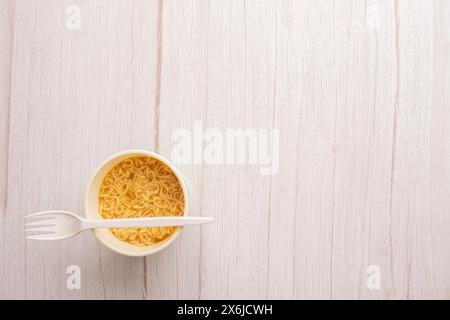 Übersicht über eine Schüssel mit Instant-Pasta-Suppe mit einer Kunststoffgabel auf hellgrauem Hintergrund. Mittagessen. Fastfood-Konzept Stockfoto