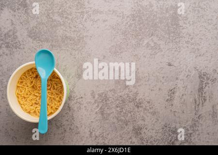 Übersicht über eine Schüssel mit Instant-Pasta-Suppe mit einem Löffel auf hellgrauem Hintergrund. Mittagessen. Fastfood-Konzept Stockfoto