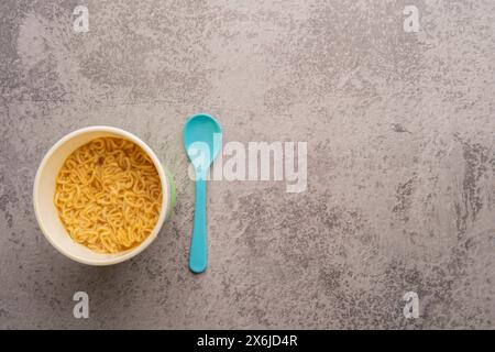 Übersicht über eine Schüssel mit Instant-Pasta-Suppe mit einem Löffel auf hellgrauem Hintergrund. Mittagessen. Fastfood-Konzept Stockfoto