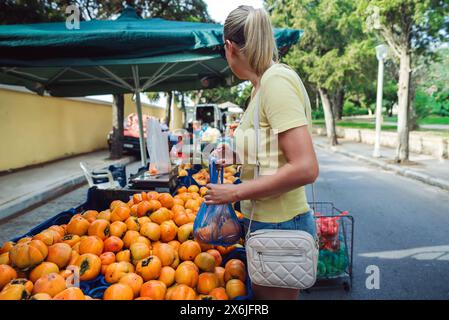 Frau auf einem Bauernmarkt kauft Persimmonen. Stockfoto