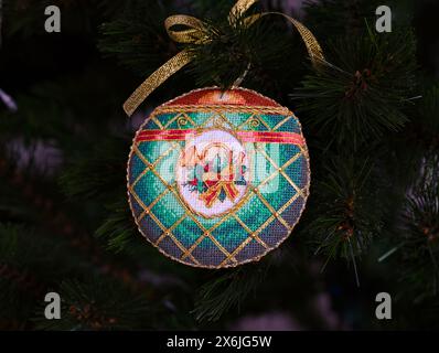 Ein kreuzgenähtes zeitloses Weihnachtsschmuck auf einem Weihnachtsbaum. Dieses grüne Weihnachtsschmuck mit Horn, Pflanze und Schleife bestickt und m Stockfoto