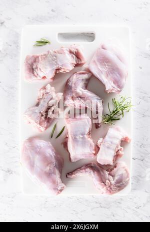 Portioniertes rohes Kaninchen mit Rosmarin auf einem weißen Schneidebrett Stockfoto