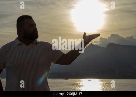 Das Bild fängt einen ergreifenden Moment ein, während ein 30-jähriger Mann vor einem atemberaubenden Sonnenuntergang steht. Der beschauliche See und die fernen Berge zusammen Stockfoto