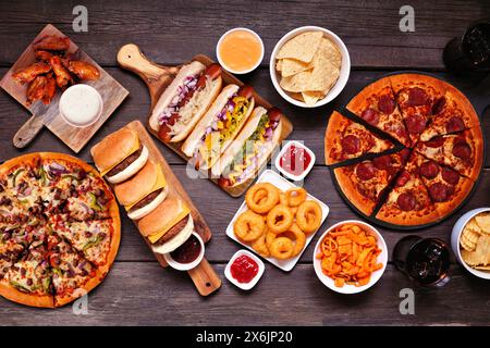 Junk Food Tischszene. Pizza, Hamburger, Chicken Wings, Hot Dogs und salzige Snacks. Blick über einem dunklen Holzhintergrund. Stockfoto