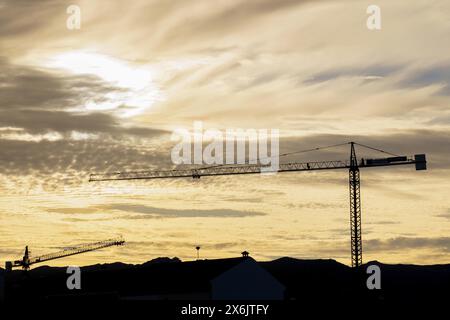 Silhouette von Kränen auf einer Baustelle mit einem bewölkten gelben Himmel, der bei Sonnenaufgang beleuchtet wird Stockfoto