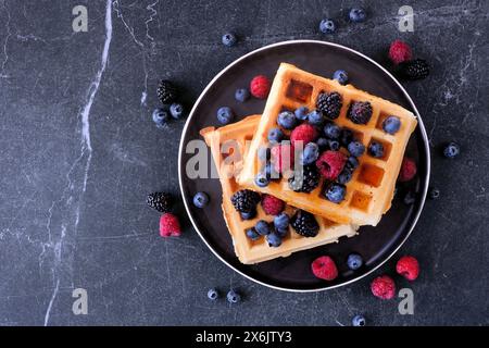 Frühstückswaffeln mit Himbeeren und Heidelbeeren. Draufsicht über einen dunklen Steinhintergrund. Stockfoto
