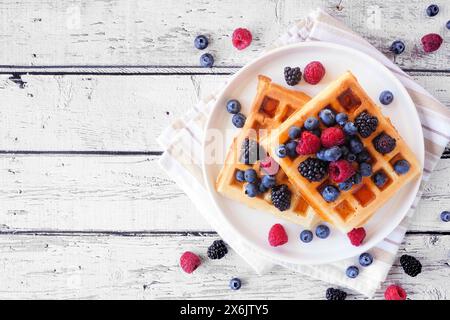 Frühstückswaffeln mit Himbeeren und Heidelbeeren. Tischszene mit Blick von oben auf weißem Holzhintergrund. Stockfoto