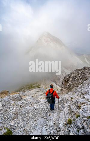 Bergsteiger, der auf einem felsigen Bergweg absteigt, bewölkter Berggipfel, Abstieg vom Gipfel des Großen Kinigat, Karnischer Main Ridge, Karnische High Stockfoto