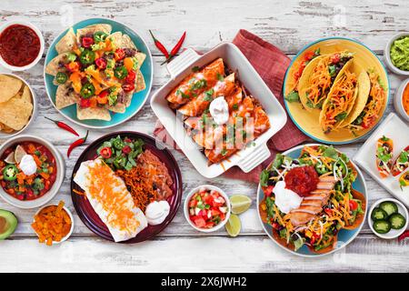 Mexikanische Tischszene. Draufsicht auf weißem Holzhintergrund. Tacos, Burrito-Teller, Nachos, Enchiladas, Tortilla-Suppe und Salat. Stockfoto