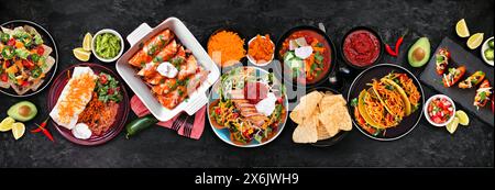 Mexikanische Tischszene. Ansicht von oben nach unten auf einem dunklen Steinbannerhintergrund. Tacos, Burrito-Teller, Nachos, Enchiladas, Tortilla-Suppe und Salat. Stockfoto